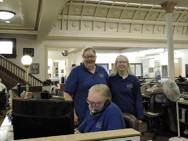 Photograph of three library employees at the Information and Reference desk on the second floor of the Piqua Public Library.