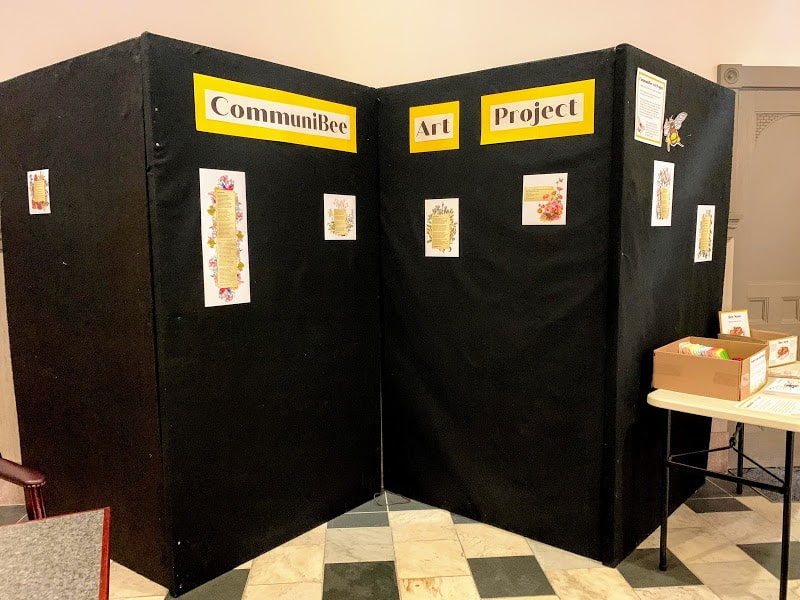Photograph of a black display board with a yellow sign on it for the CommuniBee Art Project.