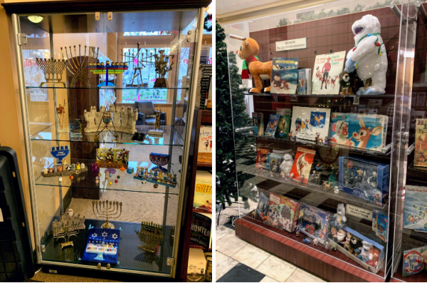 Two photographs, each of a glass display case in the Piqua Public Library. The first one has a collection of menorahs and dreidels, used in the celebration of Hanukkah. The second one has memorabilia, books, and music from the movie Rudolph the Red-Nosed Reindeer.