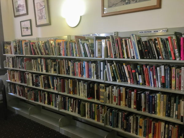 Photograph of a long row of bookshelves in the Piqua Library bookstore. The books are nonfiction and cover a variety of topics from cookbooks to travel to antiques.