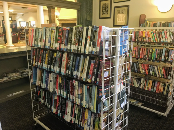 Photograph of two bookshelves on wheels in the Piqua Library bookstore. The books are novels in the mystery, Christian fiction, and teen/young adult genres.