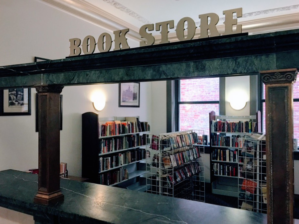 Photograph of the Piqua Public Library Bookstore. The bookstore is in what was the check in counter when the building was a hotel. The counter is a dark green marble and book shelves are visible in the background.