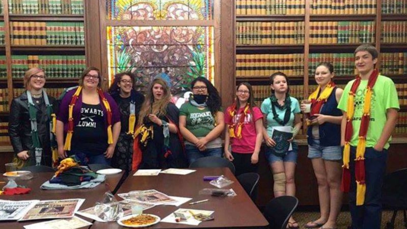 Photograph of a group of teens and library staff during summer reading. Everyone is wearing Hogwarts style scarves.